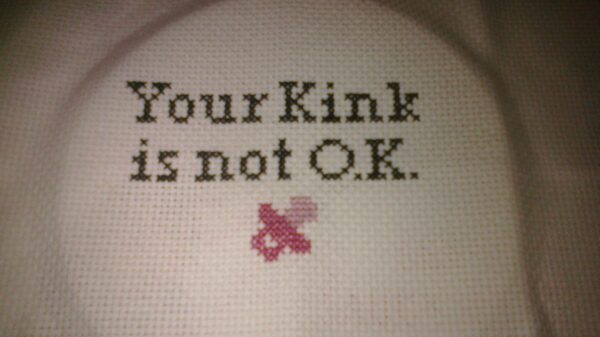 A cross stitch that says "Your Kink is not O.K."