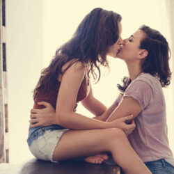 Two women in casual attire kiss. 