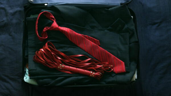 A folded black suit with red tie and red whip laying on top. 