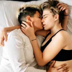 Two women lie in bed kissing and embracing. 