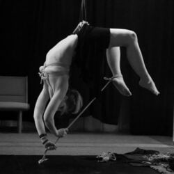 Black and white artistic image of person suspended upside down with ropes 