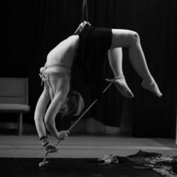 Black and white artistic image of person suspended upside down with ropes 