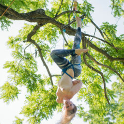 A woman dangling topless upside down in a tree
