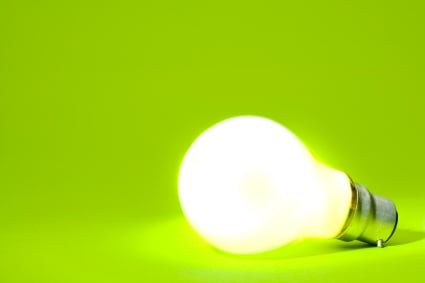 A lit lightbulb on its side with a green background.