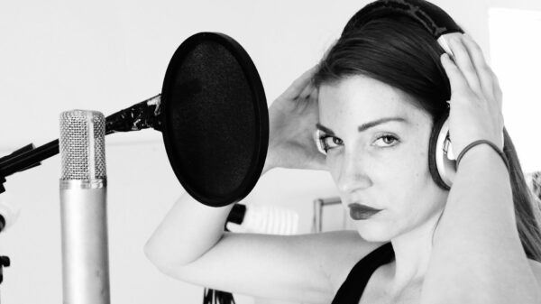 A woman holding headphones to her ears standing in front of a microphone. 