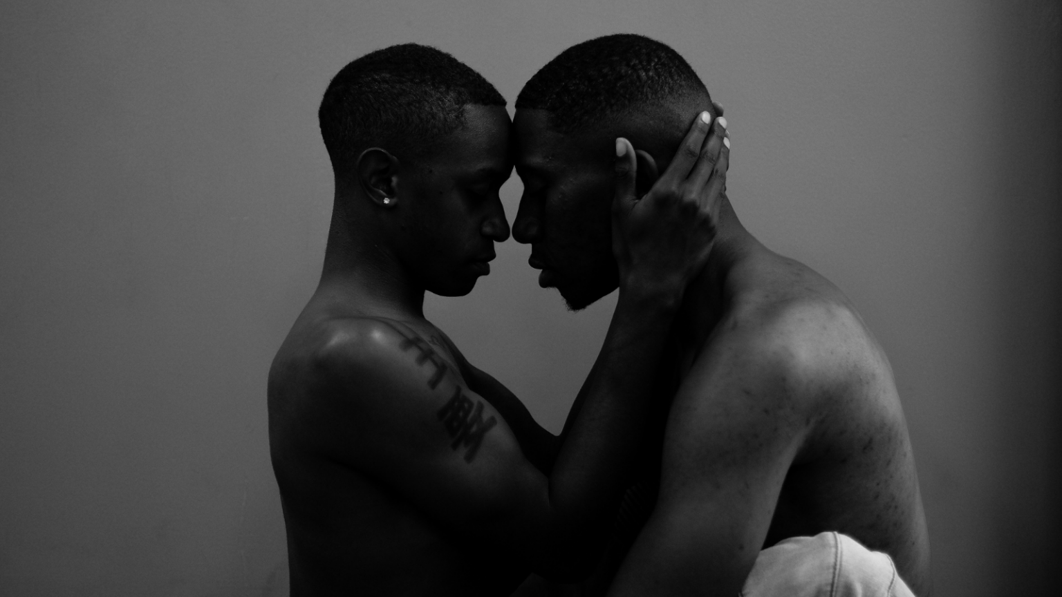 Two Black men embrace with their faces close to each other