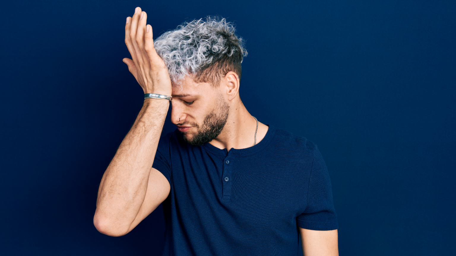 Masculine looking person with short, dyed hair with their palm on their forehead