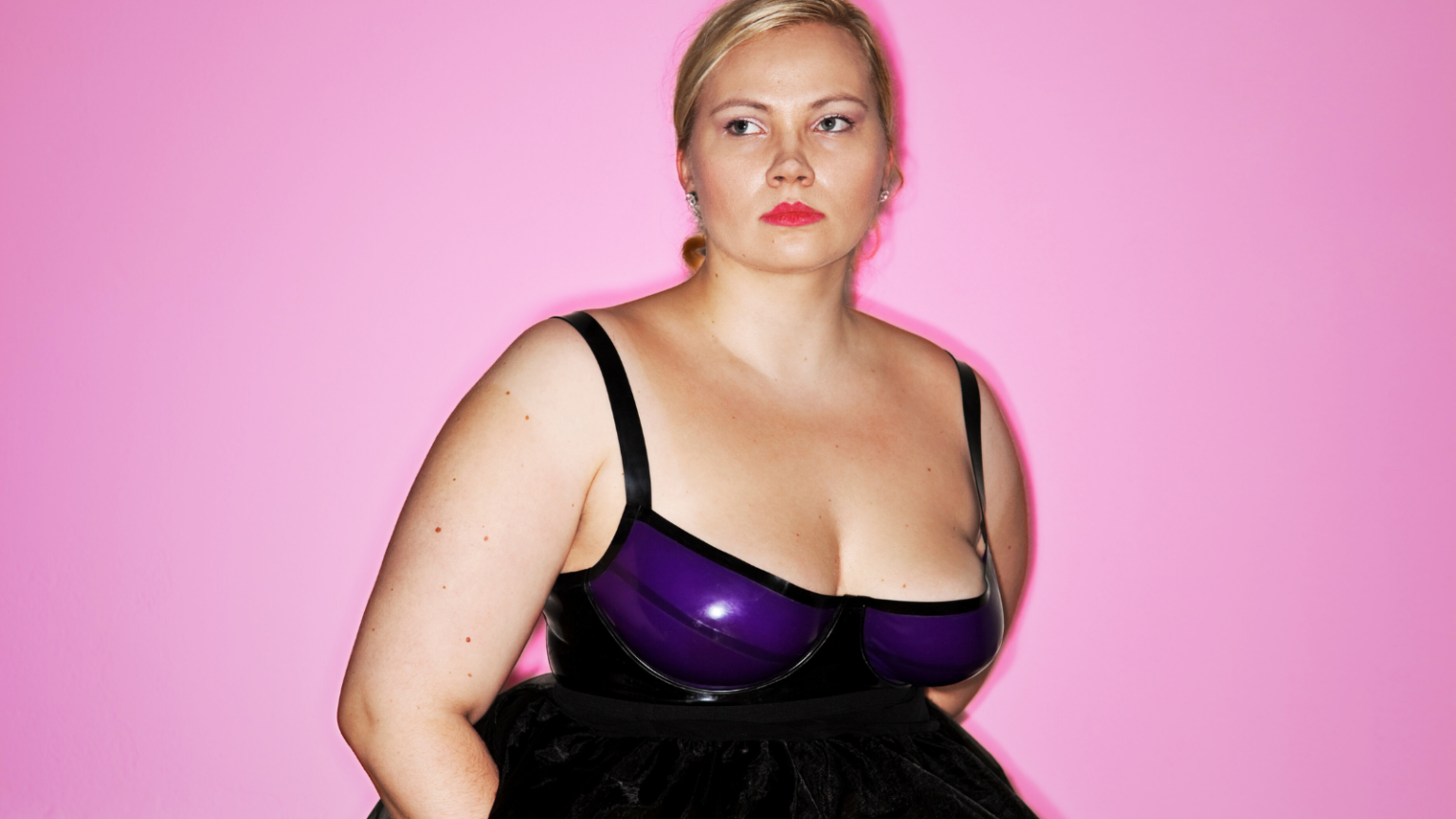 Photo of a feminine looking plus size person with light skin wearing a latex tank top