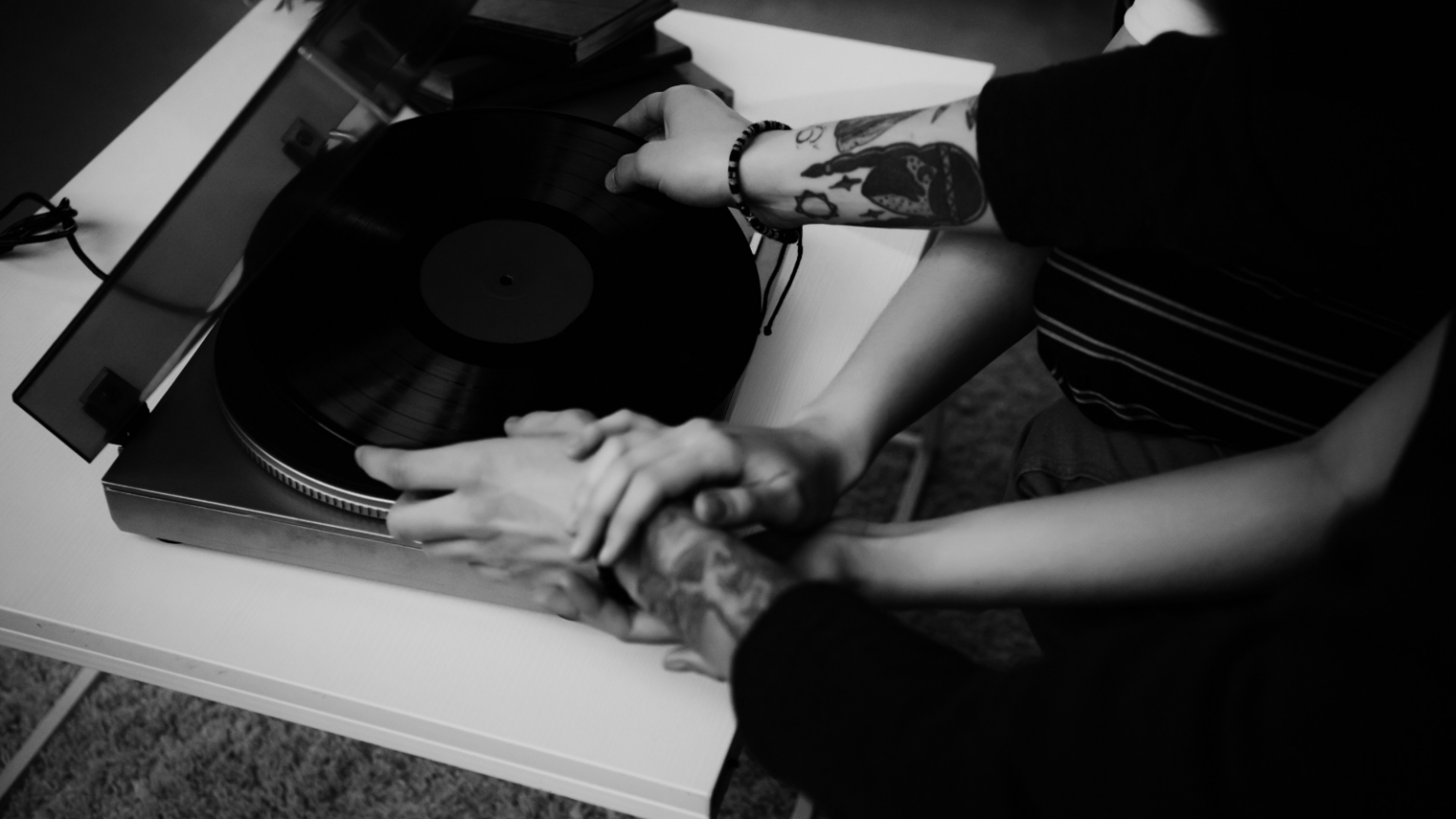 Photo of two pairs of arms reaching out to a record player
