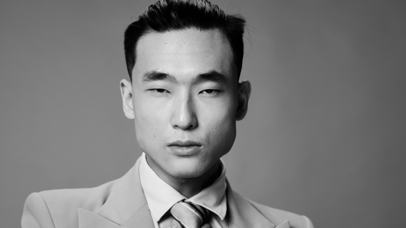 Photo of a masculine Asian person wearing a suit and looking sternly at the camera