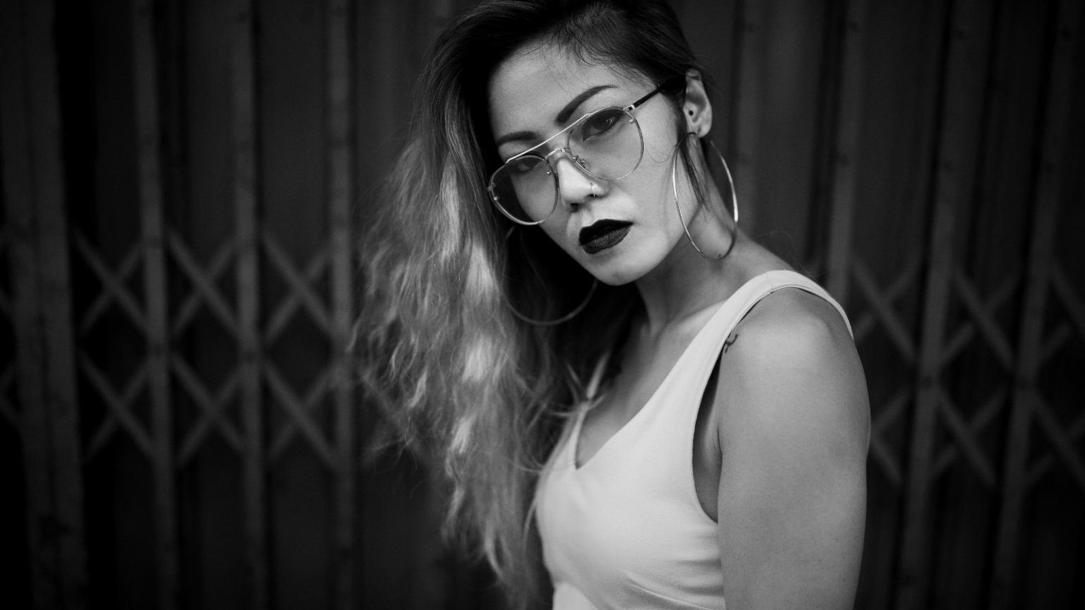 Photo of a feminine Asian person with black lipstick and glasses looking sternly at the camera