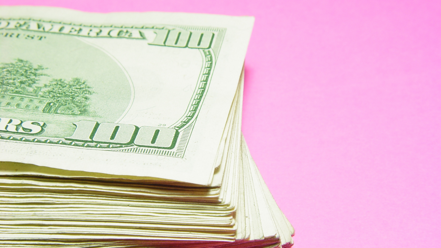 Photo of a stack of $100 bills on a pink background