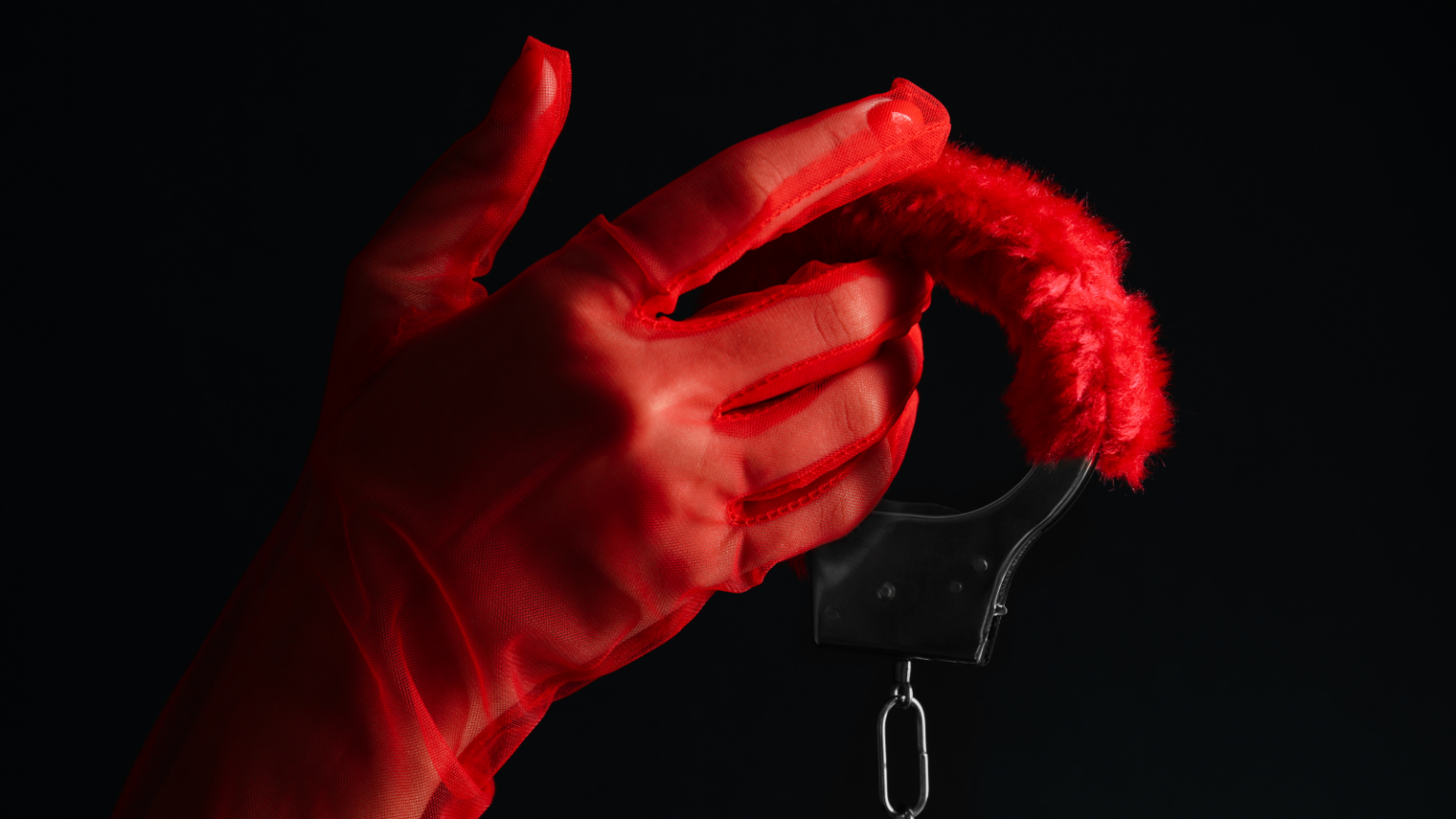 Photo of a feminine looking hand wearing a sheer red glove and holding handcuffs with fuzzy red fur on the wrists.