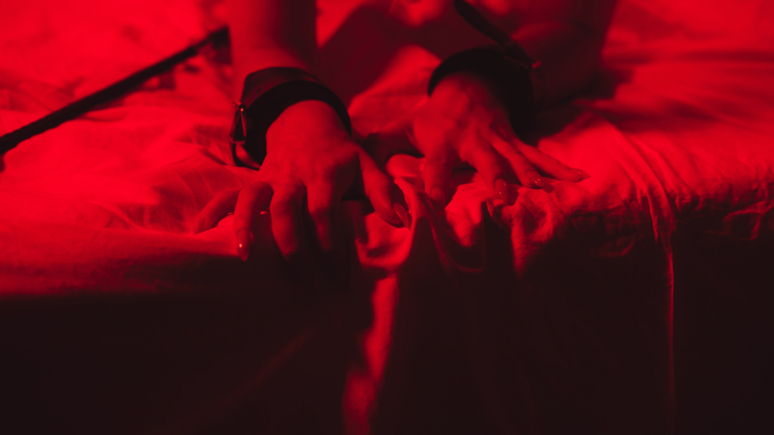 A feminine looking person's hands on a bed with handcuffs on