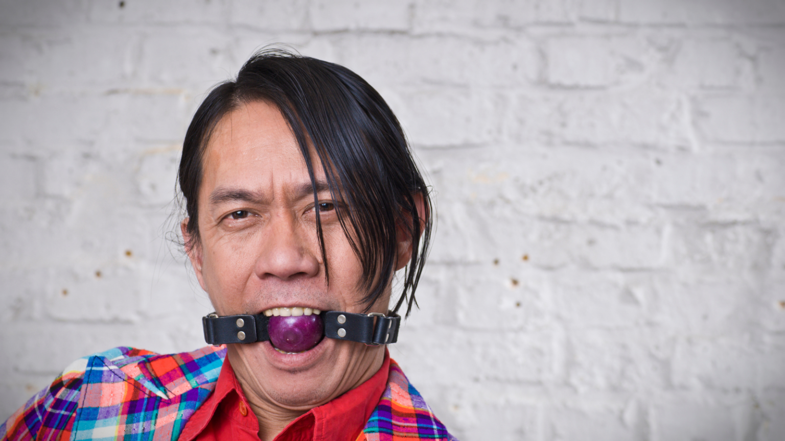 Asian man wearing plaid shirt with ball gag in mouth