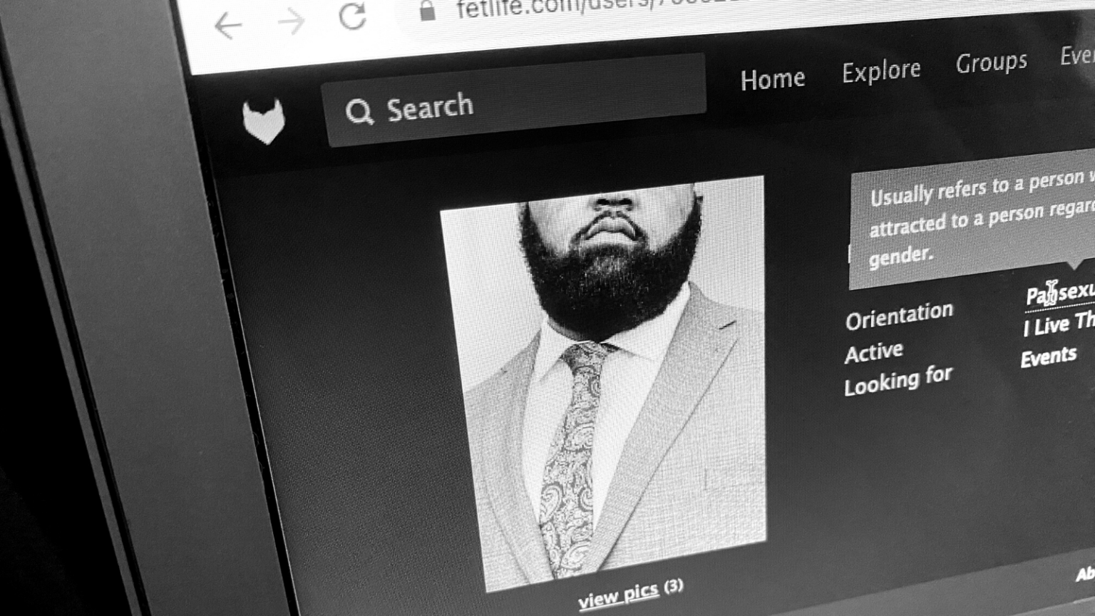 Photo of a computer screen showing the FetLife profile of a Black man with a bear wearing a suit, with his face partly cropped out