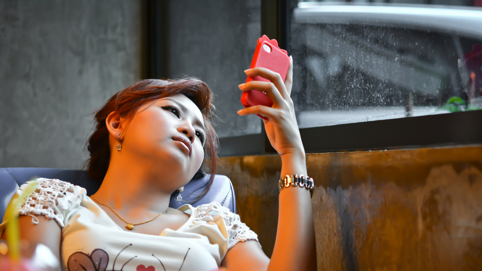 Photo of a feminine Asian person with short hair looking at phone with a mildly sad expression