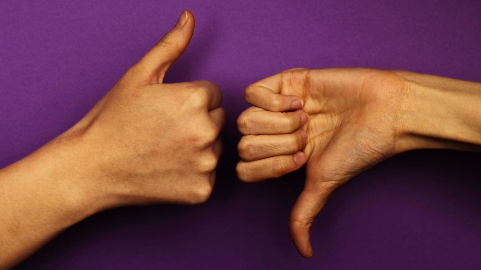 Photo of two hands with light brown skin. One is doing a thumbs up and the other is doing a thumbs down